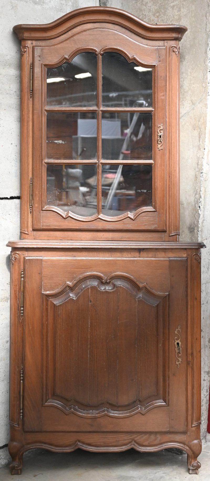 Eikenhouten tweedelige hoekvitrine in Régencestijl met één paneeldeur onderaan en een beglaasde deur bovenaan. XIXde eeuw.