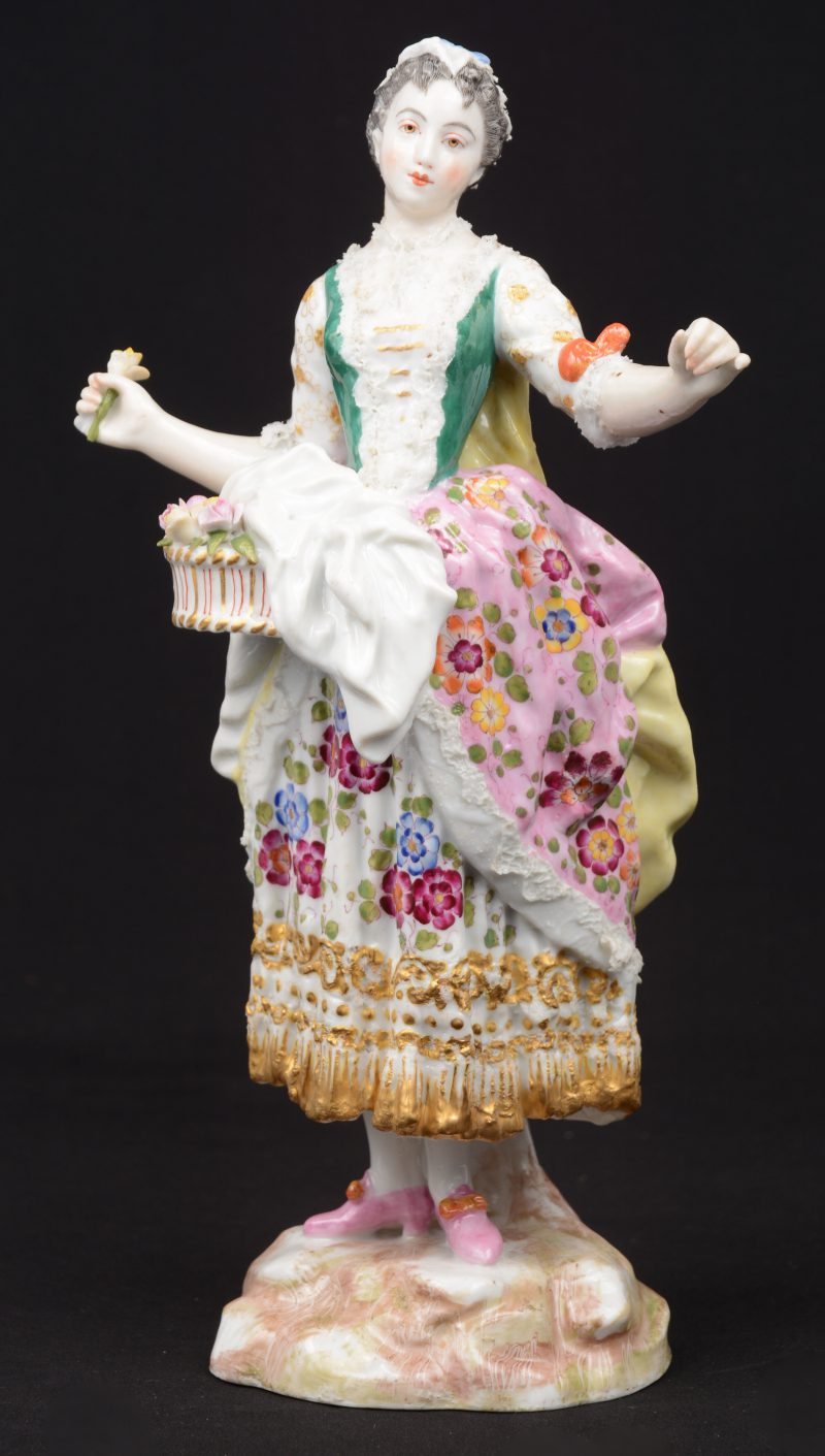 “Jonge vrouw met bloemen”. Een beeldje van meerkleurig Duits porselein. Gemerkt met gekruiste degen. Enige schade aan de jurk. XIXe eeuw.