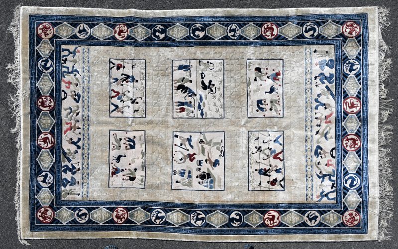 Een handgeknoopt Chinees tapijt van wol en zijde met diverse voorstellingen met personages en dieren in het decor.