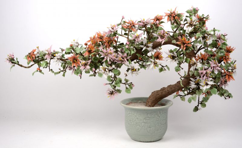Een bloeiende plant met bloemen en blaadjes van jadeiet en in pot van Celadonkleurig porselein.