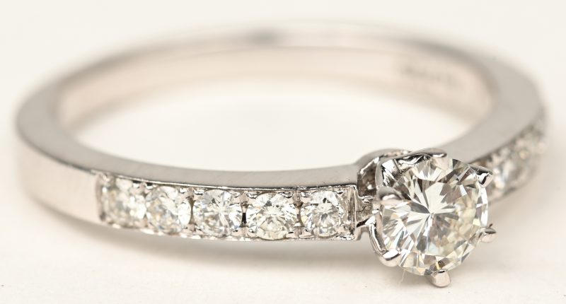 Een 18 K witgouden ring bezet met een centrale briljant van +- 0,25 ct. en briljanten met een gezamenlijk gewicht van +- 0,30 ct.