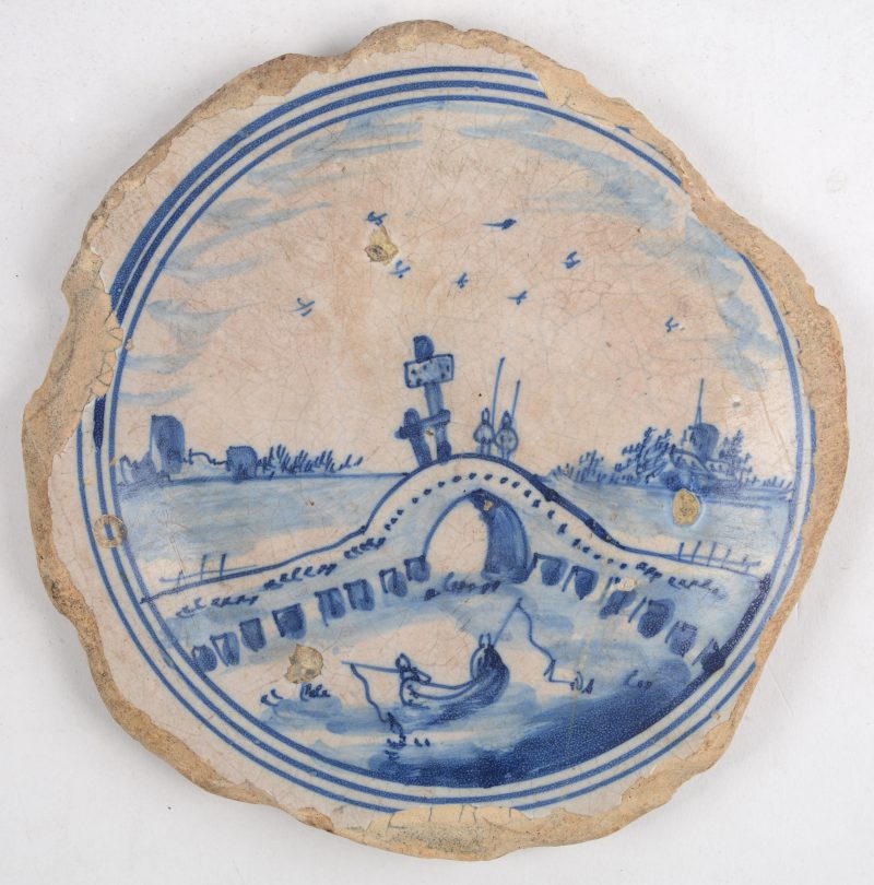 Een ronde tegel van Delfts aardewerk met een blauw op wit landschapsdecor. Randschade. XVIIe eeuw.