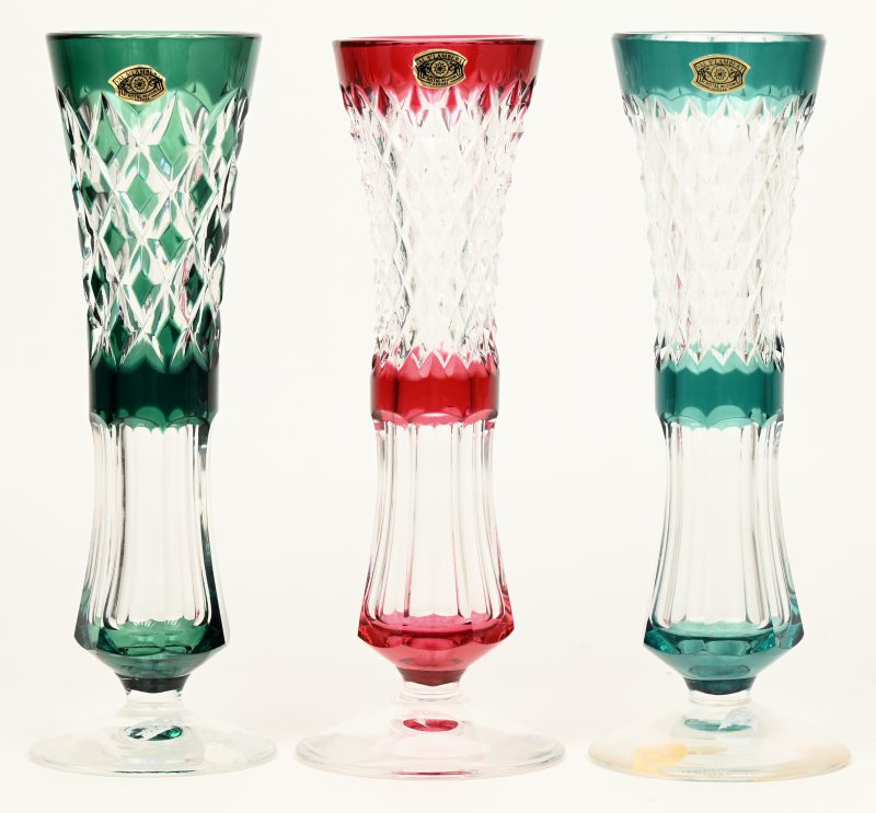 Drie geslepen kristallen fluitvaasjes op voet, model Solignac, waarbij twee groene en een rode. Allen gemerkt en in originele doos.