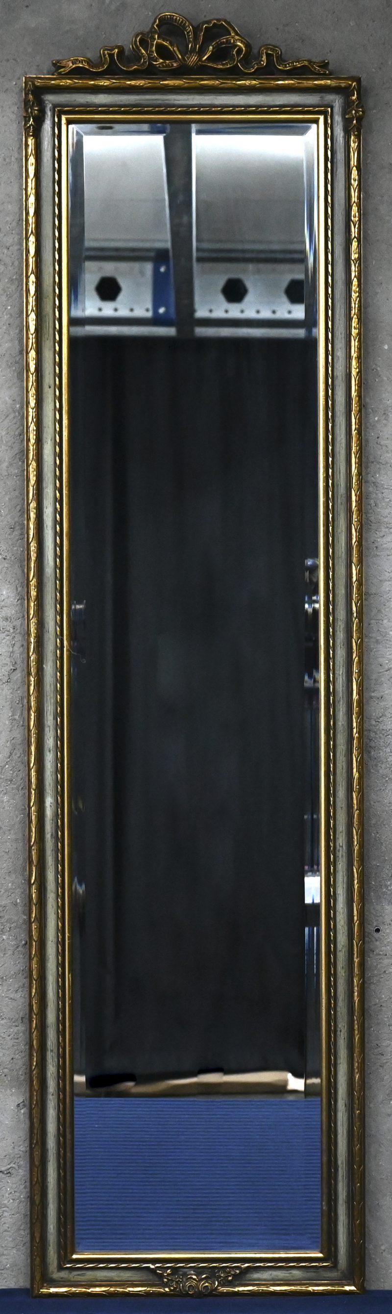 Een langwerpige spiegel met bovenaan een strikmotief en onderaan een kleine guirlande, deels verguld.