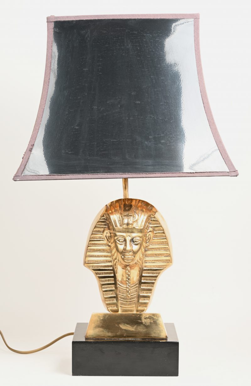 Een lampvoet, versierd met een verguld koperen voorstelling van het masker van Toetanchamon op een zwart houten basis.