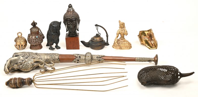 Een gevarieerd lot koperen voorwerpen bestaande uit: een hoofdje van een boeddha, een olielampje, een uil, een zittende boeddha, een bel, een polsband, een potje, een massagespin, een geldbuidel en een hoorn in de vorm van een drakenkop.
