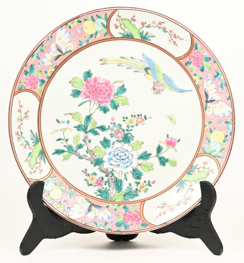 Een bord van Chinees porselein met een meerkleurig decor van bloeiende struiken, vogels en vlinders. Onderaan gemerkt.