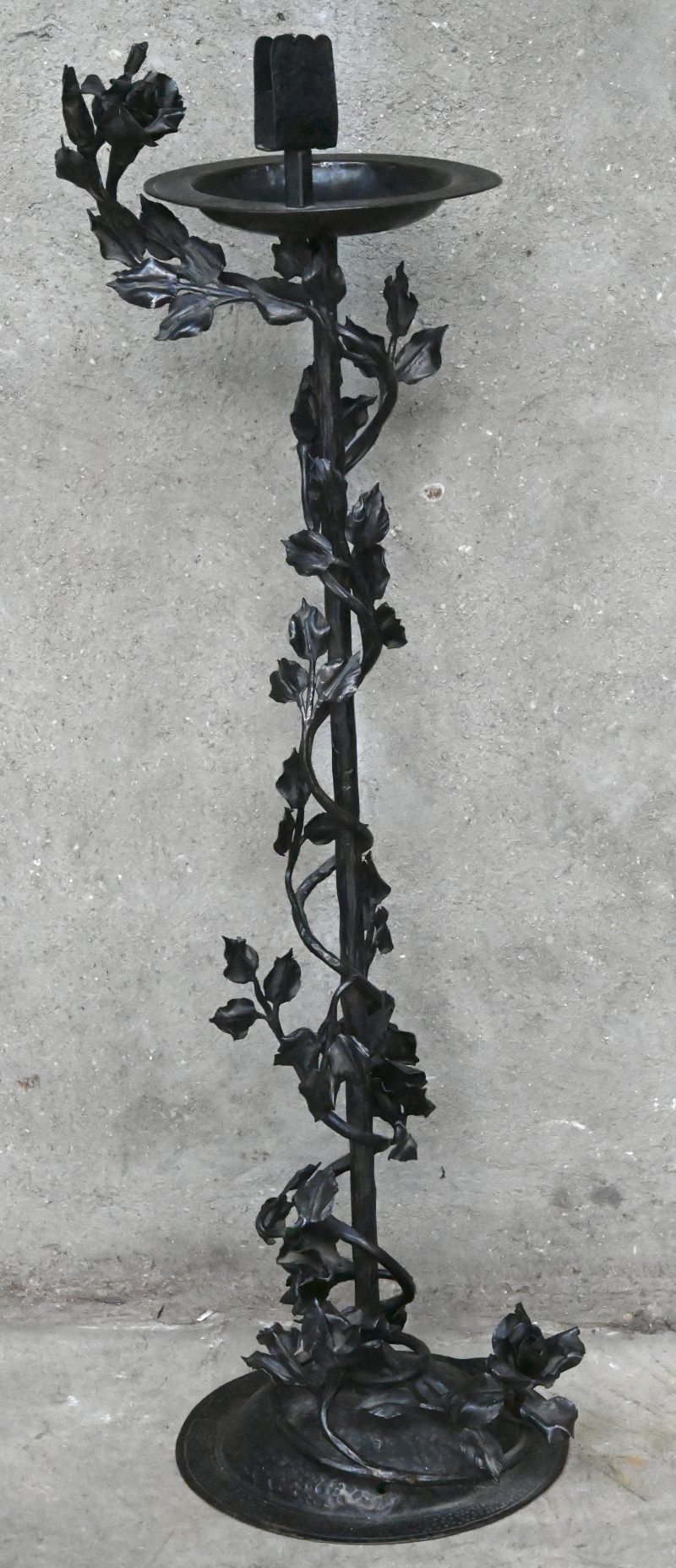 Een staande asbak van smeedijzer met luciferhouder, versierd met rozenranken.