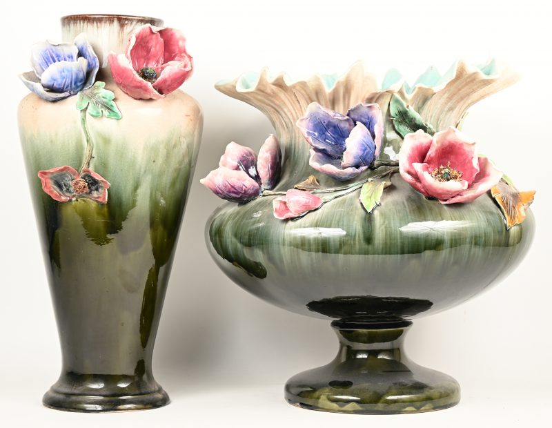 Twee verschillende grote vazen van geglazuurd Belgisch/ Duits aardewerk, versierd met bloemen in hoogreliëf. Meerdere beschadigingen.