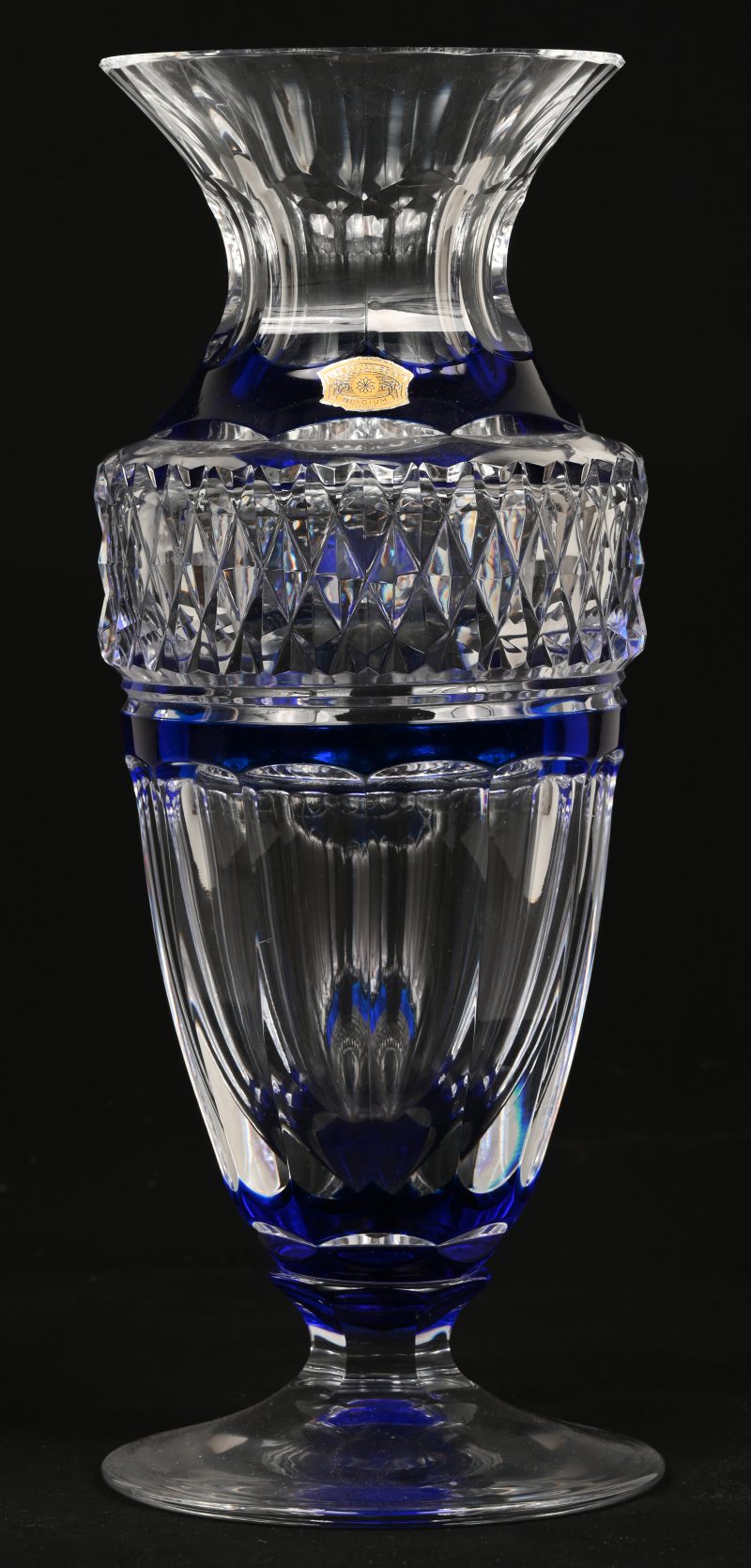Een kristallen vaas met vernauwende hals en met rond voetstuk. Deels in de massa blauw gekleurd. Gemerkt met label en onderaan. P.U.