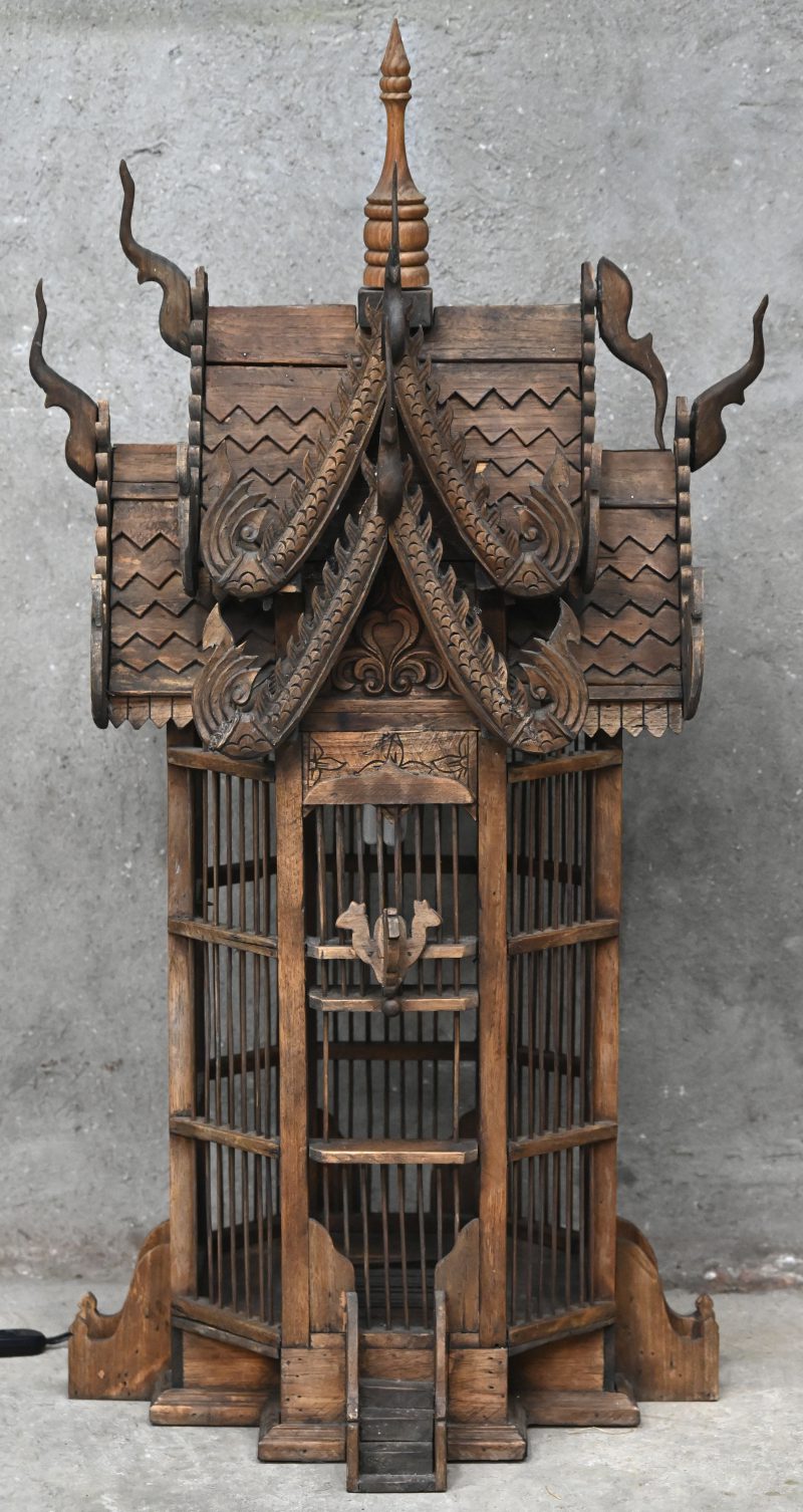Een houten vogelkooi met gebeeldhouwd pagodedak.