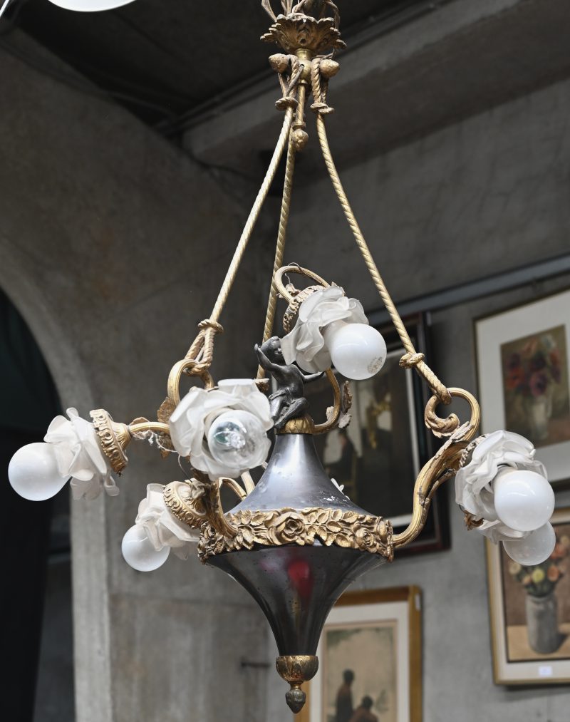 Een antieke koperen luchter met zeven lichtpunten met bloemvormige glazen kapjes.
