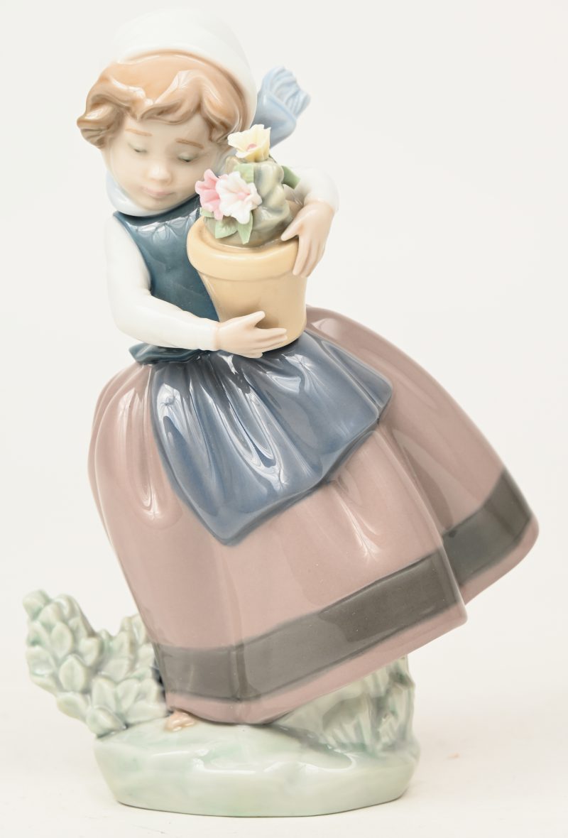 “Meisje met bloempot”. Een beeldje van meerkleurig Spaans porselein. Onderaan gemerkt en gedateerd 1983.
