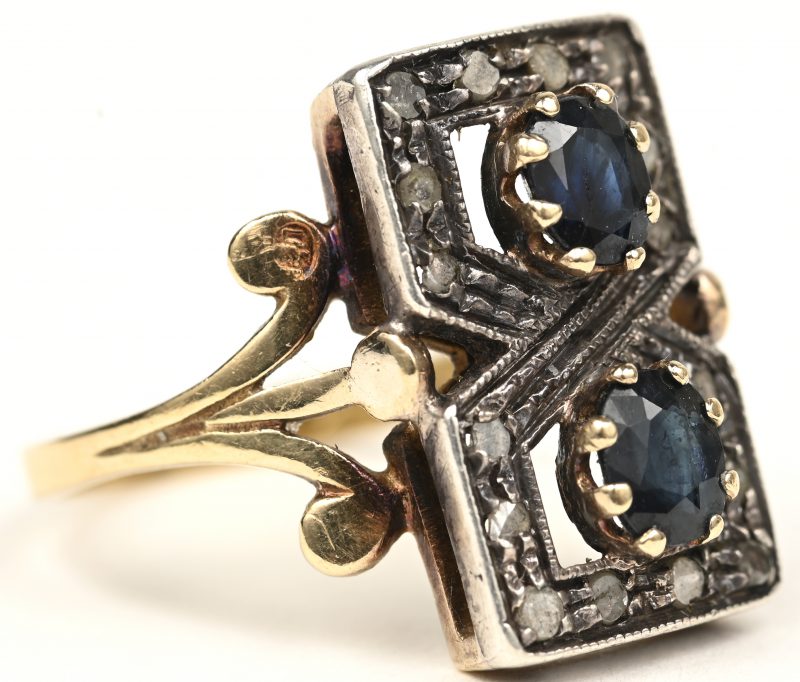 Een ring van 18 K geel goud en zilver bezet met een twee saffieren met een gezamenlijk gewicht van +- 0,50 ct. en kliene diamanten oude slijp met een gezamenlijk gewicht van +- 0,16 ct.