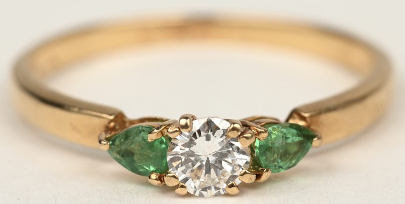Een 18 K geelgouden ring bezet met twee smaragden in markies geslepen met een gezamenlijk gewicht van +- 0,20 ct. en een centrale briljant van +- 0,25 ct.