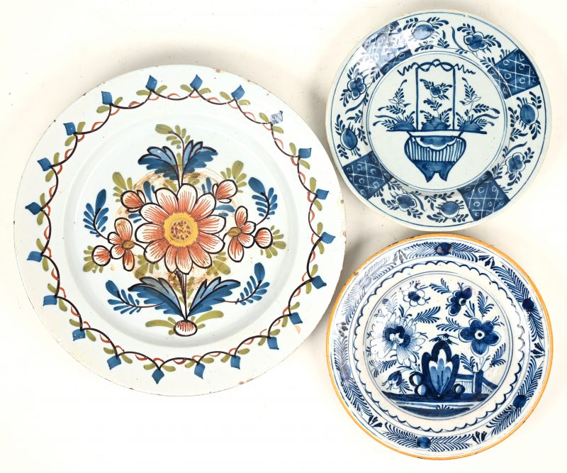 Een lot van drie antieke Hollands aardewerken borden, waarbij één met blauw bloemendecor en gele rand, één naar Chinees voorbeeld en één met meerkleurig bloemendecor. Laatste met haarscheur.