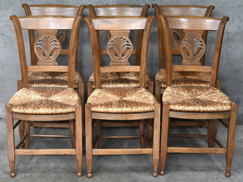 Een reeks van zes houten stoelen met gesculpteerde versiering van palmtakken in de rug. Met rieten zitten.