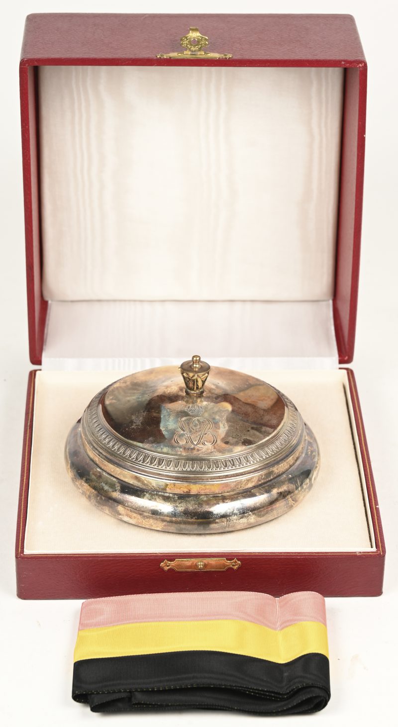 Een 835‰ zilveren doopschaal met deksel. Met lint in Belgische driekleur en in originele doos met gekroonde BF. Geschenk vanwege Boudewijn en Fabiola voor de geboorte van een zevende kind.