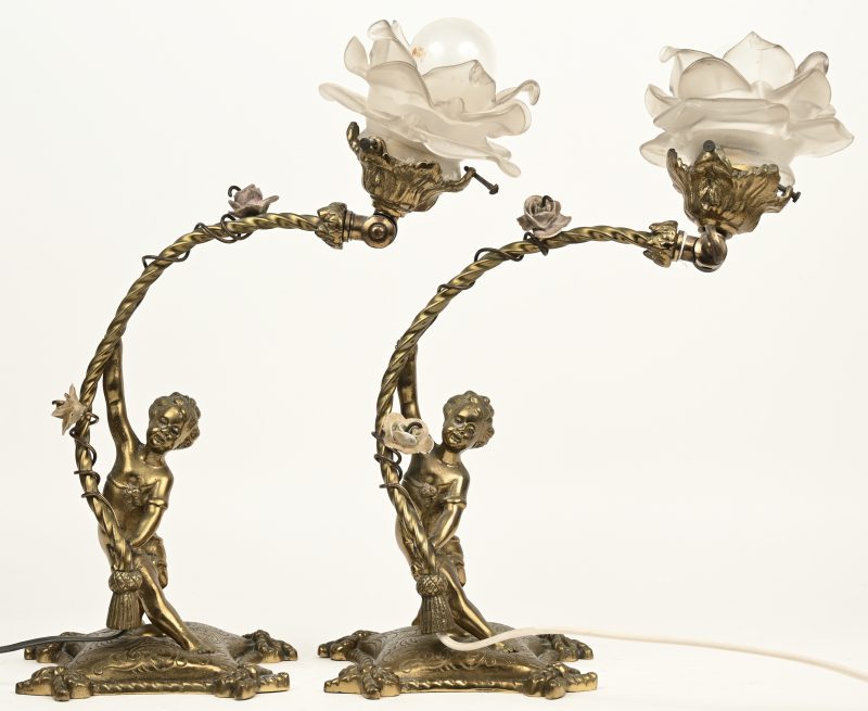 Een paar verguld bronzen lampjes met kantelbare lichtpunten, gedragen door putti en versierd met porseleinen bloempjes. De kapjes licht bezchadigd.