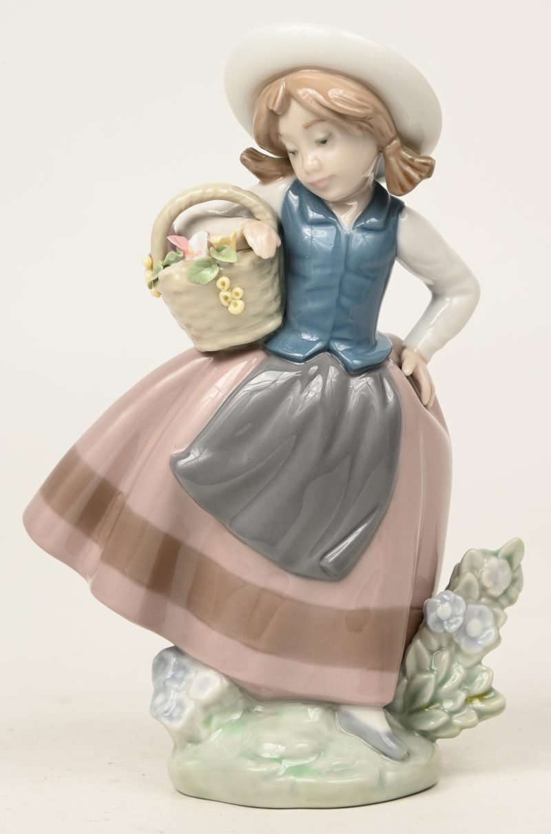 “Meisje met bloemenmand”. Een beeldje van meerkleurig Spaans porselein. Gemerkt en gedateerd 1983. Enkele bloemblaadjes beschadigd.