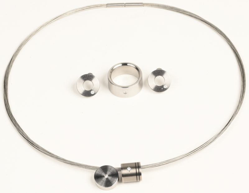 Een 10 rijen halsketting, ring, oorbellen en hanger van metaal en één hanger van titanium bezet met briljanten met een gezamenlijk gewicht van +- 0,20 ct.