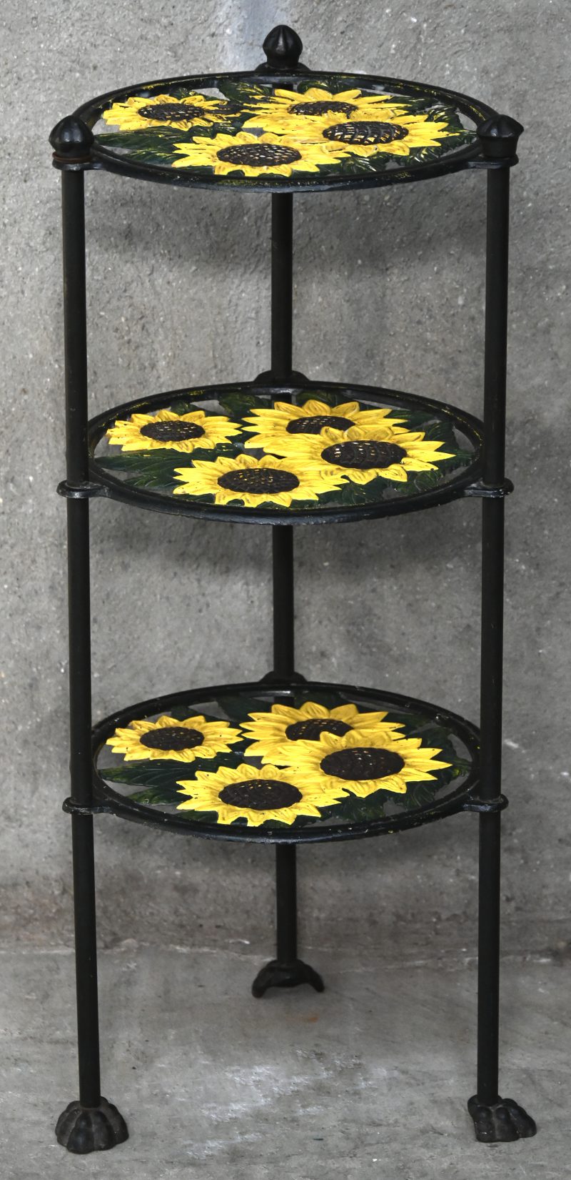Een gepolychromeerd gitijzeren staander in drie niveaus met decor van zonnebloemen.