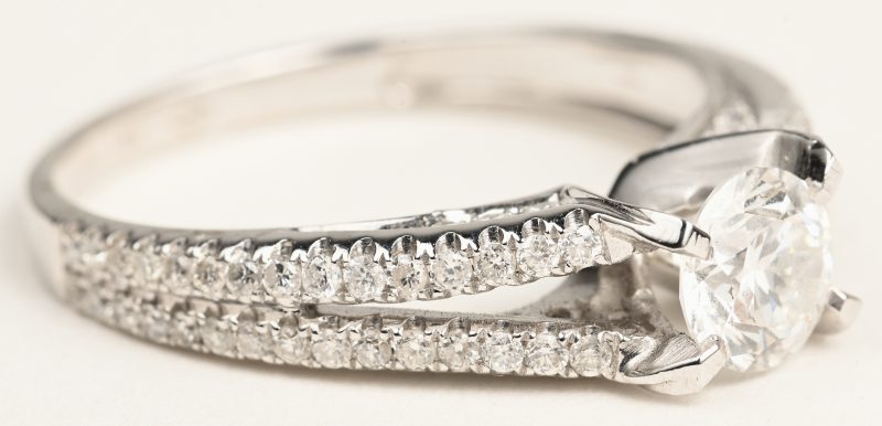 Een 18 K witgouden ring bezet met een centrale briljant van +- 0,64 ct. en briljanten een gezamenlijk gewicht van +- 0,66 ct.