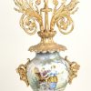 Een driedelig Italiaans klokstel van vmeerkleurig aardewerk met plattelandscènes in het decor, verwerkt in verguld bronzen monturen en versierd met engeltjes, saterkoppen enz.