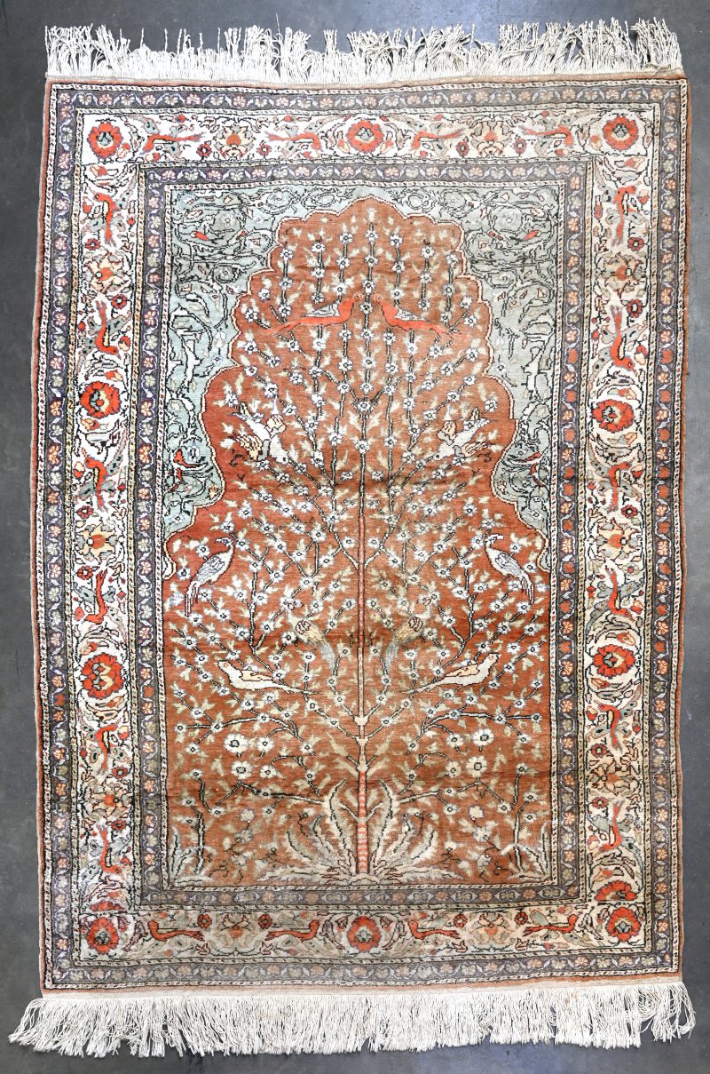 Een handgeknoopt Perzisch wollen tapijt. met in het decor een bloeiende boom met vogels.