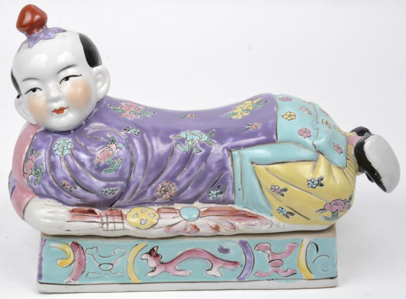Een Chinese neksteun/dekseldoos in van meerkleurig porselein in de vorm van een liggend kind.
