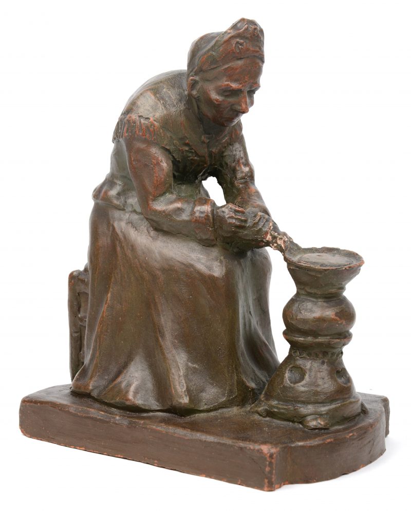 “Vrouw aan de stoof”. Een beeldje van gepatineerd terracotta. Gesigneerd met stempel.