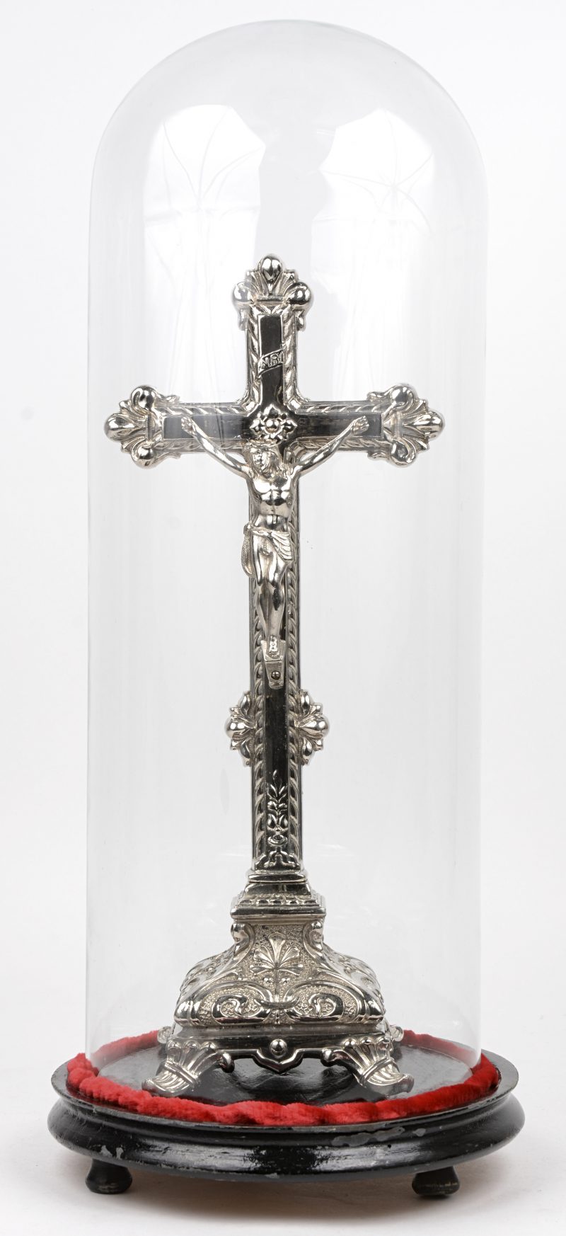 Een kruisbeeld van verzilverd metaal onder glazen stolp met houten sokkel.