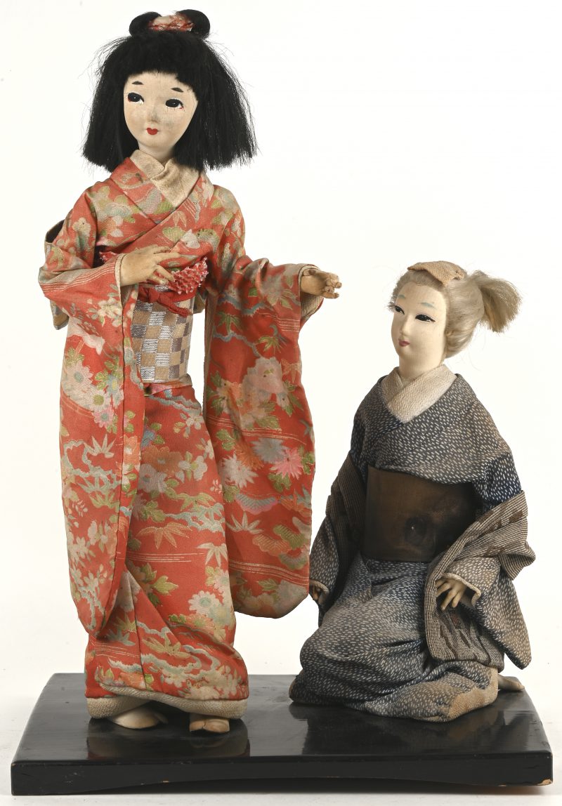 Twee Japanse geishapoppen op houten voetstuk.