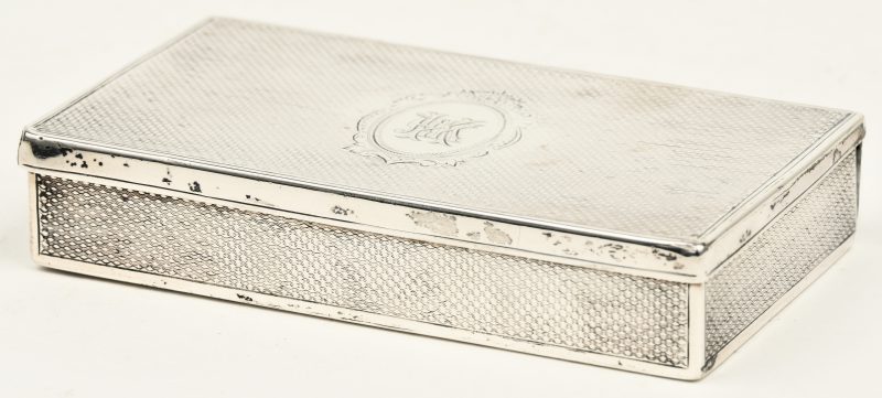 Een rechthoekige sigarettendoos van geguillocheerd zilver met een centraal monogram. Dubbele scharnieren, enige slijtage. Keuren van Birmingham, datumletter g voor 1881, makersmerk Colen Hewer Cheshire.
