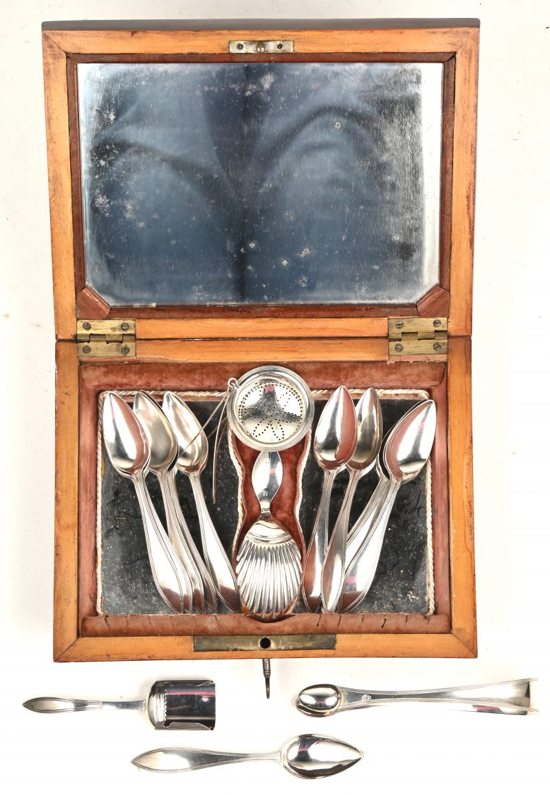Een notenhouten theekistje met spiegeltjes op vier bolpootjes met daarin twaalf theelepeltjes met Nederlandse keuren, tweede gehalte datumletter B voor 1832, een suikertang en theezeefje en twee diverse schepjes, eveneens Nederlands zilver.