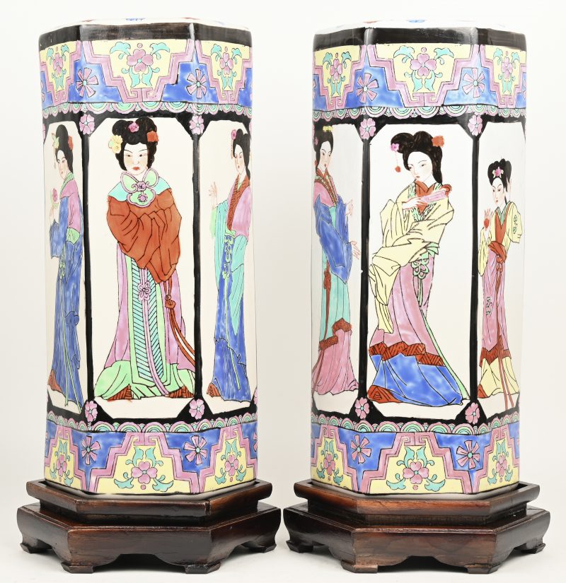 Een paar zeshoekige vazen van Chinees porselein met meerkleurig decor van geisha’s. Op houten sokkels.