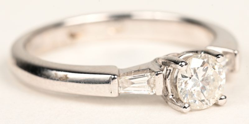Een 18 K witgouden ring bezet met één centrale briljant van +- 0,44 ct. en met diamant baguettes met een gezamenlijk gewicht van +- 0,12 ct.