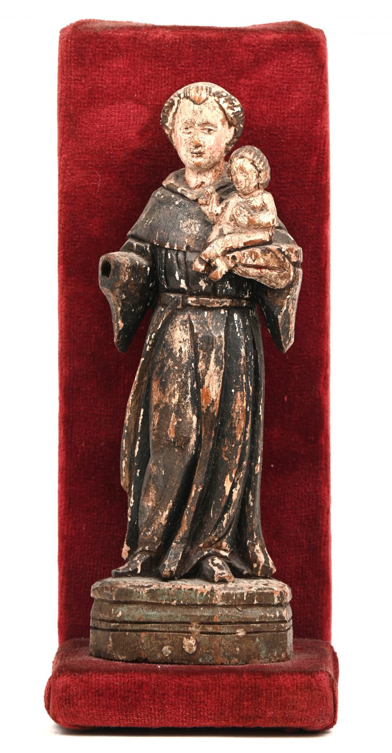 Een klein gepolychromeerd houten beeldje van een monnik met het Kind Jezus op de arm. Mogelijk nog XVIIIde eeuw. Een arm manco, slijtage.