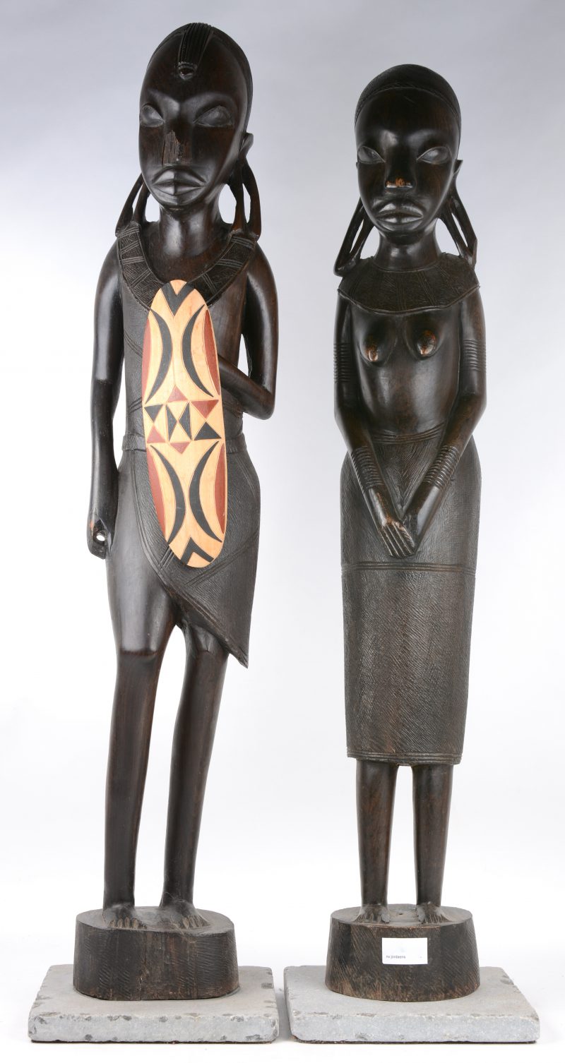 Twee Afrikaanse houten beelden op stenen voetstuk.