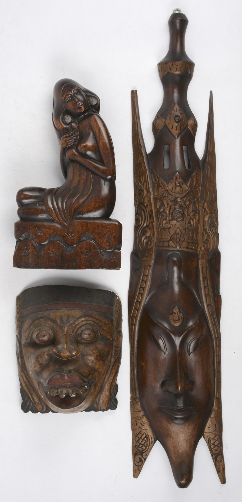 Een lot Aziatisch houtsnijwerk, bestaande uit een beeldje van een zittend naakt en twee maskertjes.