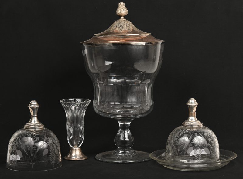 Een lot bestaande uit een glazen coupe, twee glazen stolpjes waarvan één met een onderzetter en een glazen vaasje. Allen met details van verzilverd metaal.