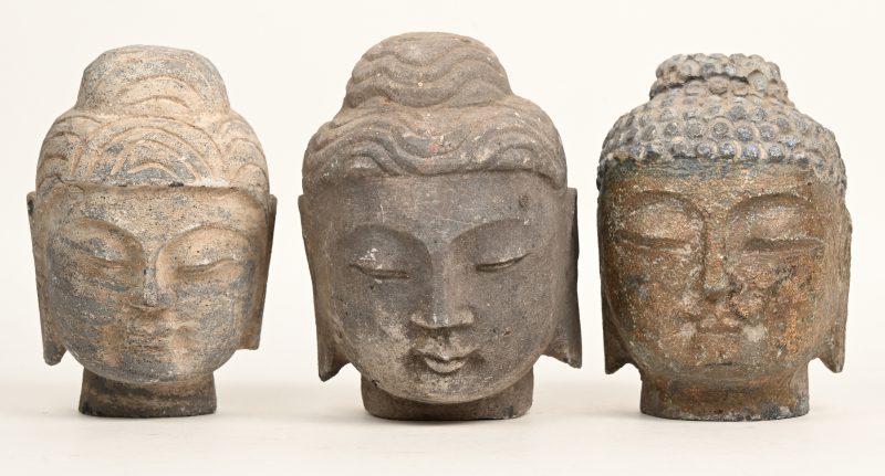 Drie stenen boeddhahoofden, waarvan één met sporen van verguldsel. Zuid-Oost-Azië.