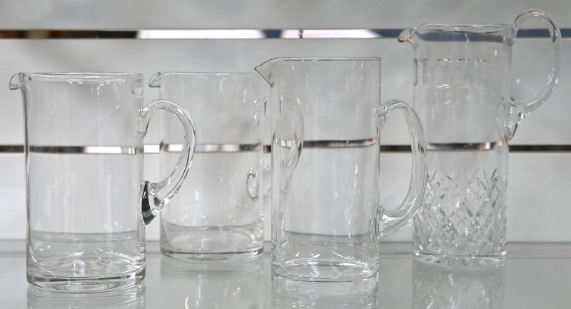 Een lot van vier kleurloos glazen schenkkannen, waarbij één met geslepen ruitmotief en een andere gemerkt van Marimekko (Finland).