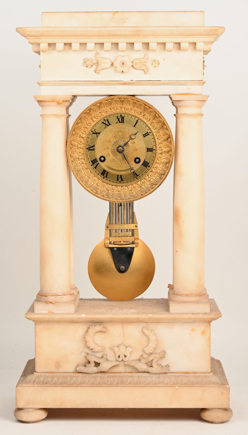 Een albasten kolompendule, klokwerk gedragen door vier Dorische zuilen. Compleet met slinger en sleutel. Kleine letsels. XIXde eeuw.