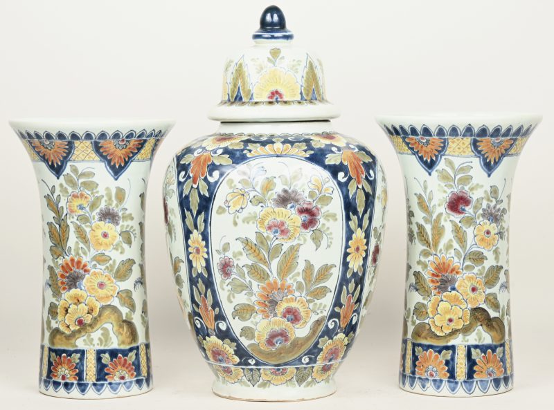 Een driedelig kaststel van meerkleurig Delfts aardewerk, bestaande uit een dekselvaas en twee kraagvazen. Gemerkt.