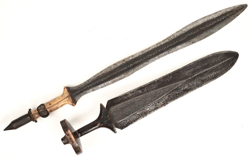 Twee Afrikaanse korte zwaarden. Het ene met houten heft (50 cm), het andere met een heft van hoorn en metaal (68 cm).