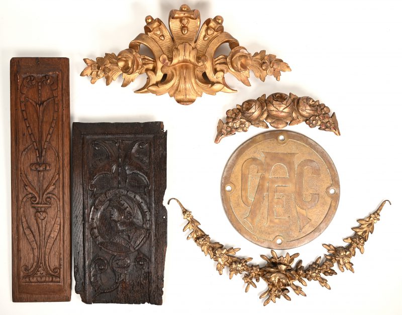 Zes diverse sierstukken. Drie diverse guirlandes van verguld gips, een gebeeldhouwd meubelpaneel uit de XVIIde eeuw en eentje uit het einde van de XIXde eeuw. We voegen er een grote ronde koperen plaquette met logo van CAEC (?) aan toe.