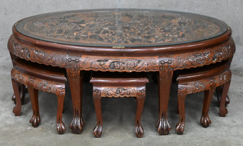 Een lage gebeeldhouwd hardhouten tafel met zes stoeltjes. Het blad versierd met een uitgestoken krijgsscène onder glas.