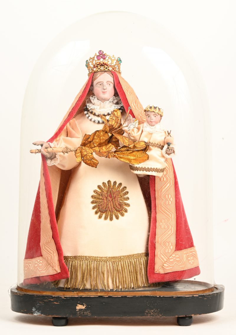 Een Madonna en Kind onder stolp. Gepolychromeerd hout. Met kleding van flueel o.a. kant. Met vergulde palmtak.