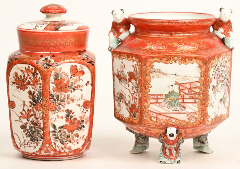 Een lot van twee Japans porseleinen potjes. Rood gekleurd met vergulde details en met illustraties en gedragen door figuren. Het kleinere met deksel en onderdeksel. Omstreeks 1900.